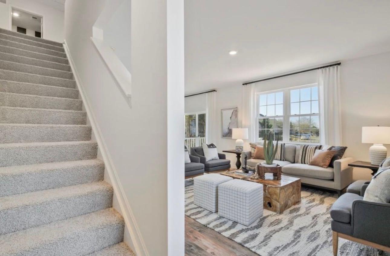 The Frederick Retreat living room viewed from the staircase, with a grey sofa, dark armchairs, ottomans, and a wood-slab coffee table on a patterned rug
