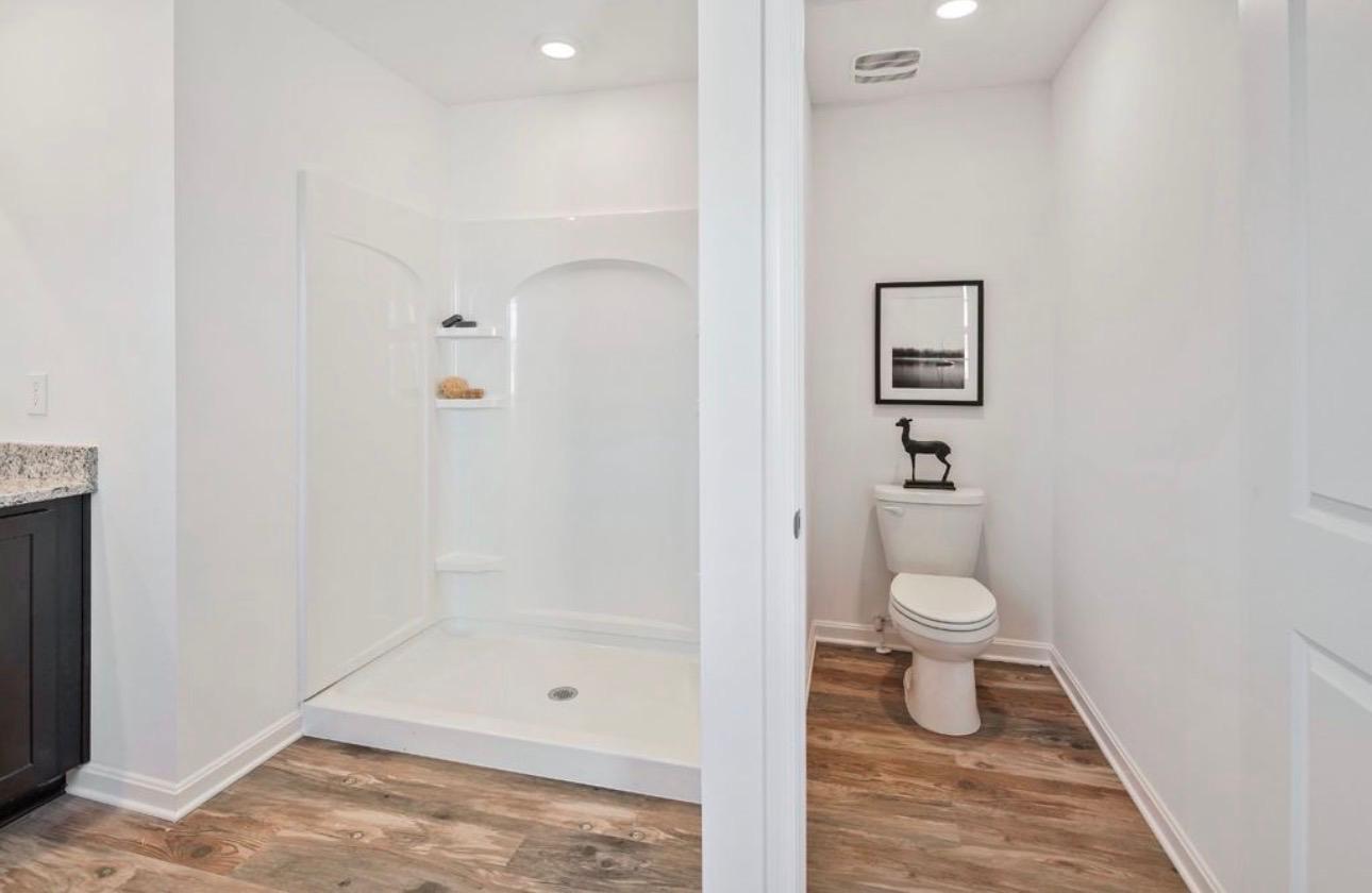 The Frederick Retreat primary bathroom showing a white one-piece shower stall and a separate toilet alcove with black-framed art on the wall