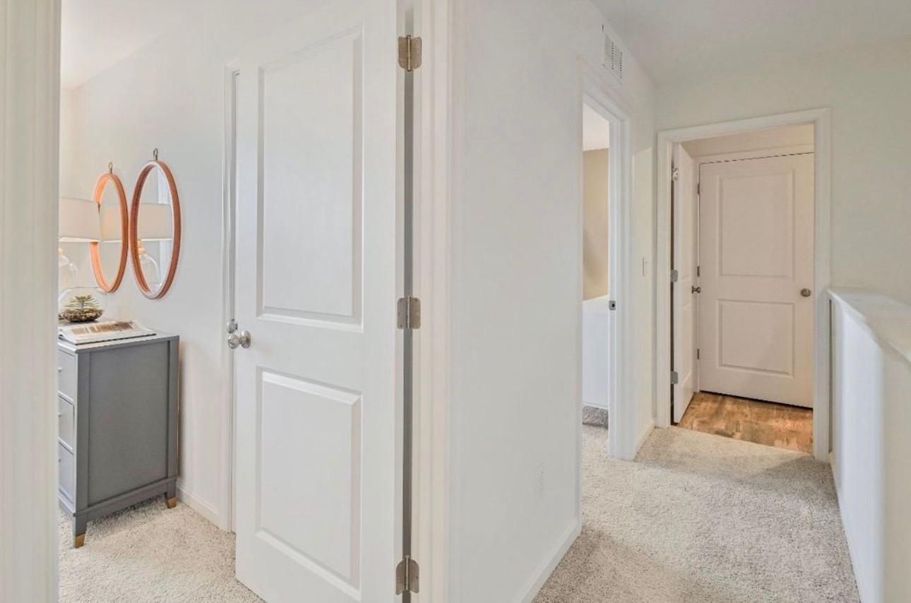 The Frederick Retreat hallway looking toward multiple bedroom doorways with a dresser and framed mirrors visible