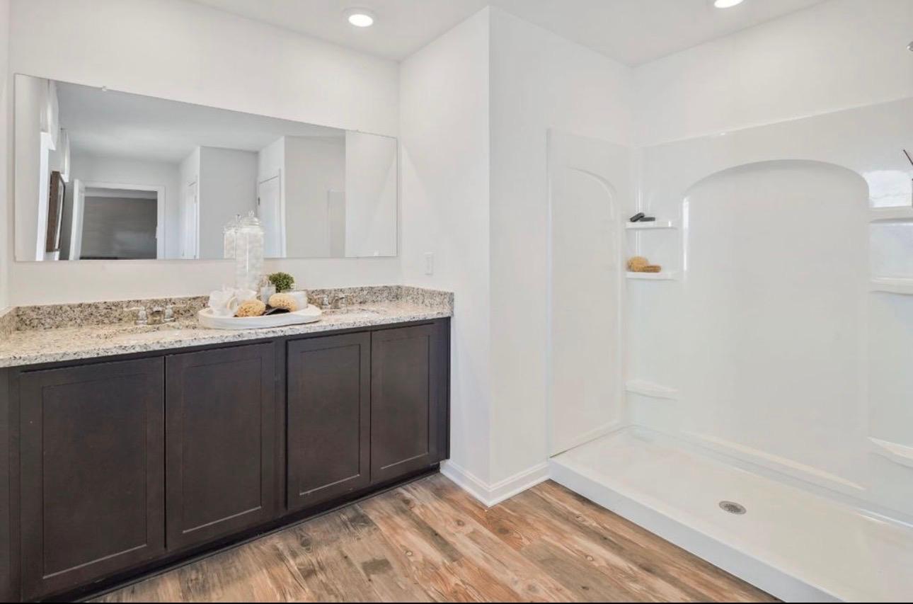 The Frederick Retreat primary en-suite bathroom with a dark espresso double vanity, speckled granite countertop, large frameless mirror, and a white one-piece shower unit