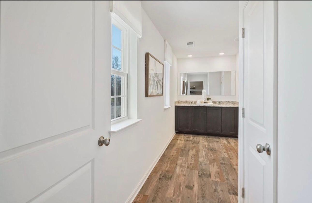 The Frederick Retreat primary bathroom vanity at the end of a hallway, with dark espresso cabinets, a speckled granite countertop, and a large frameless mirror